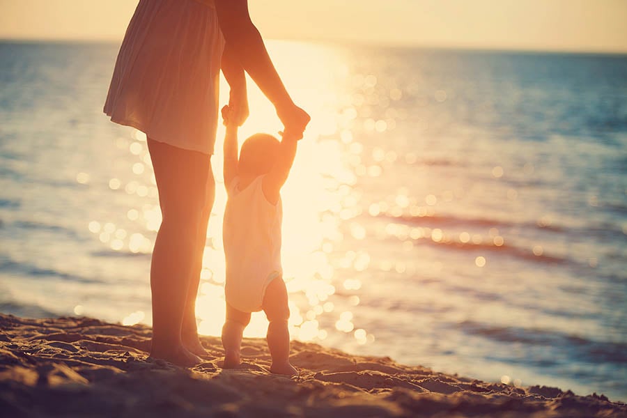 Mother and baby playing on the beach at sunset | Travel Nation