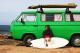 A surfer sat in the ground in front of a green campervan